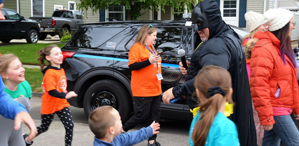 Angell students running at Fun Run event and giving Principal Gigliotti dressed as Batman a high five