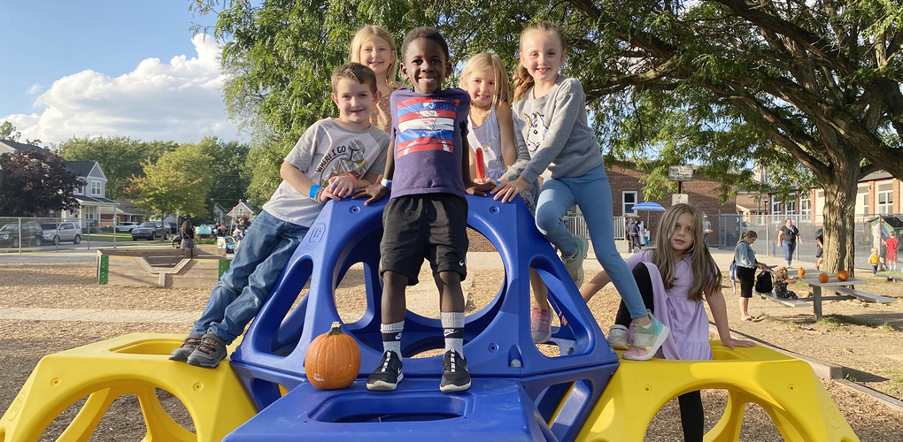 Angell students at fall festival standing on playscape smiling
